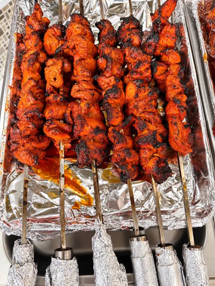 Six skewers of charred chicken tikka fresh off the grill